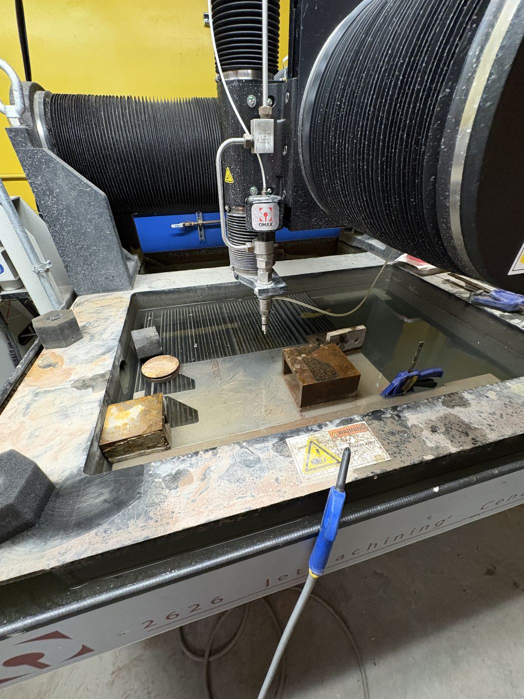 Parts being cut on the OMAX waterjet, nozzle over the submerged cutting bed.
